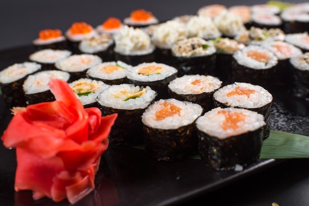 Rollos de sushi japoneses servidos en plato negro sobre fondo oscuro