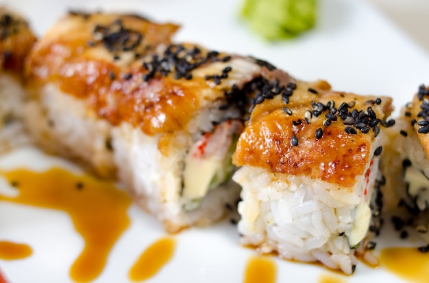 Rollos, sushi y jengibre en un plato blanco y una superficie clara.