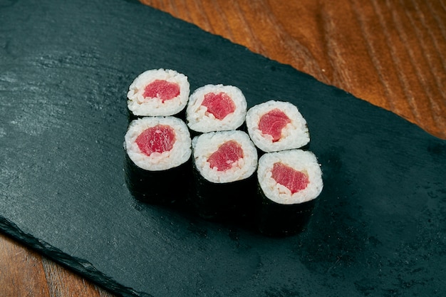 Rollos de sushi maki con atún en un tablero de pizarra negro sobre una mesa de madera. Cocina japonesa.