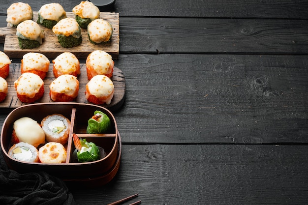 Rollos de sushi maki horneados con salmón, cangrejo, pepino, aguacate, huevas de pez volador sobre mesa de madera negra