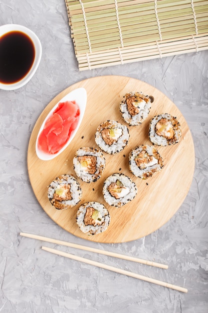 Rollos de sushi maki japonés con salmón, sésamo, pepino sobre tabla de madera sobre un fondo de hormigón gris. vista superior.