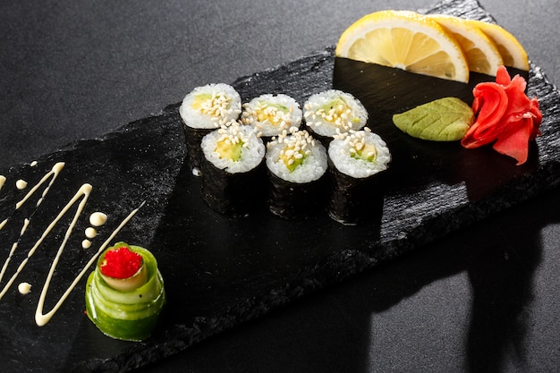 Rollos de sushi Maki con pepino o aguacate sobre piedra negra en la oscuridad