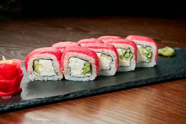 Rollos de sushi con pepino, queso philadelphia y atún en una pizarra negra sobre una mesa de madera. Cocina japonesa.