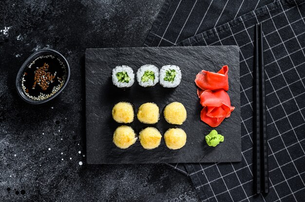 Rollos de sushi con pepino, salmón y camarones en una bandeja de piedra.