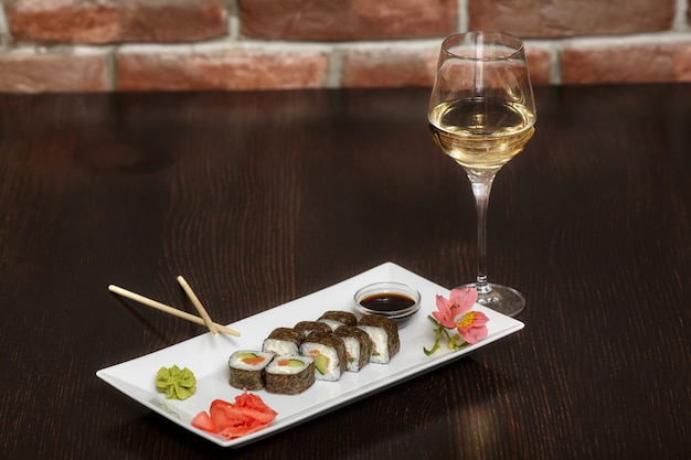 Rollos de sushi en plato blanco y copa de vino