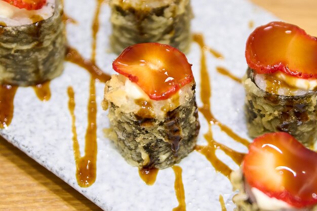 Rollos de sushi en un plato blanco con salsa de soja y fresas