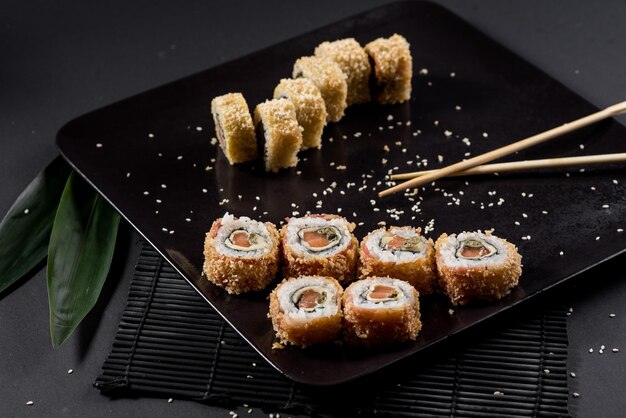 Rollos de sushi en plato negro con hojas de bambú y palillos