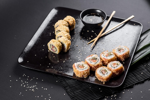 Rollos de sushi en plato negro con hojas de bambú y palillos