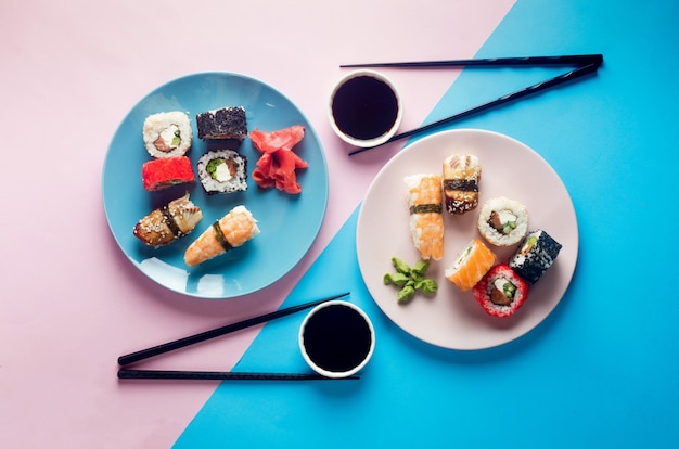 Rollos de sushi sabroso en placa azul con salsas, palillos, jengibre y wasabi sobre fondo de color. Menú de sushi. Servicio de entrega de comida japonesa. Surtido de sushi, rollos, gunkan, nigiri.