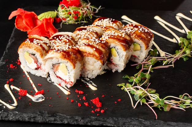 Rollos de sushi con salmón, aguacate, anguila, caviar de pez volador y queso crema en negro