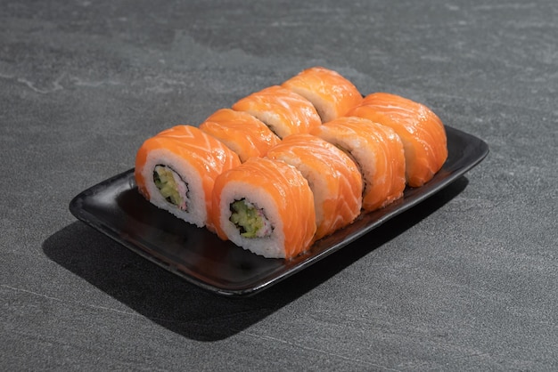 Rollos de sushi con salmón, aguacate y pepino en un plato rectangular negro sobre un fondo de pizarra de piedra negra