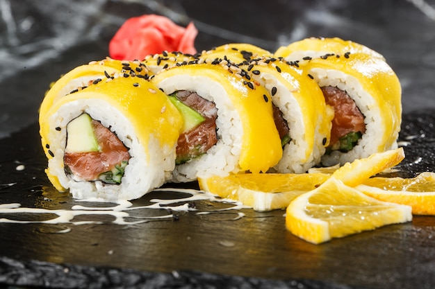 Rollos de sushi con salmón, aguacate, tortilla dentro y mango encima. Rollos de sushi con salmón sobre fondo de mármol negro. Menú de sushi Comida japonesa. Foto horizontal