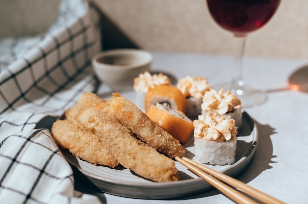 Foto rollos de sushi con salmón, crema de queso y camarones fritos en placa gris y copa de vino tinto