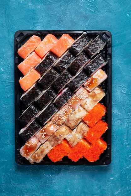 Rollos de sushi sobre un fondo de piedra azul con palos de bambú y salsa de soja