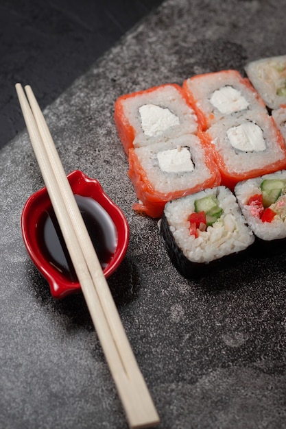 Rollos de sushi sobre un fondo de piedra oscura con palos de bambú y salsa de soja