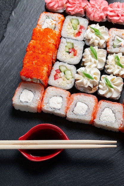 Rollos de sushi sobre un fondo de piedra oscura con palos de bambú y salsa de soja