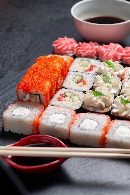 Rollos de sushi sobre un fondo de piedra oscura con palos de bambú y salsa de soja