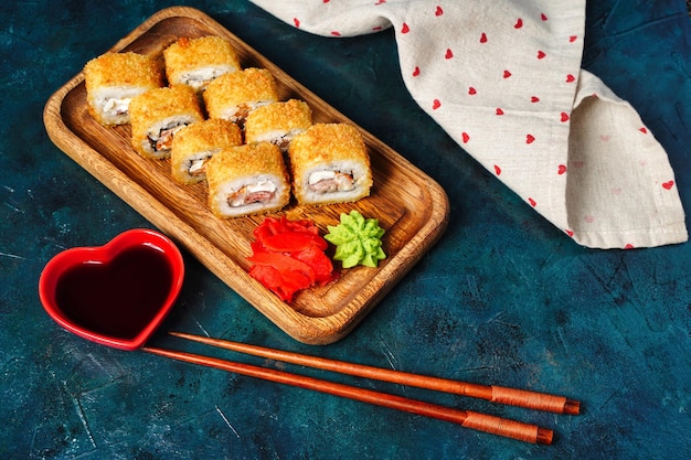 Rollos de sushi tempura fritos colocados en un plato de madera sobre fondo oscuro Comida de fusión tradicional japonesa estilo menú de restaurante bufé de degustación de fondo Foto de alta calidad