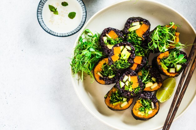 Rollos de sushi vegano con arroz negro, aguacate y camote en un plato blanco