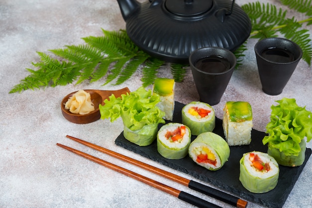 Rollos de sushi vegetariano vegetal con una tetera de té y tazas chinas de pie sobre una mesa de hormigón.