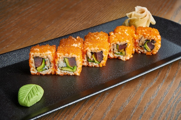 Rolo apetitoso com arroz, caviar, atum, abacate em um prato preto em um de madeira. rolos de sushi clássico japonês. frutos do mar saborosos. adicionar ruído ao po