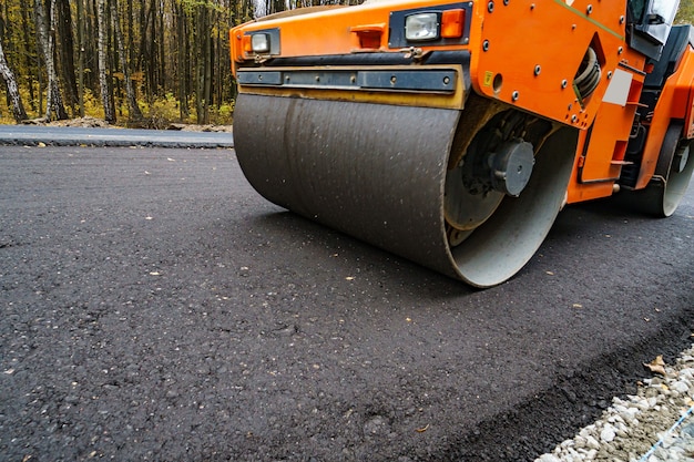 Foto rolo compactador aplainando o asfalto novo. rolo de vibração pesada no trabalho de pavimentação de asfalto, reparação de estradas. foco seletivo.