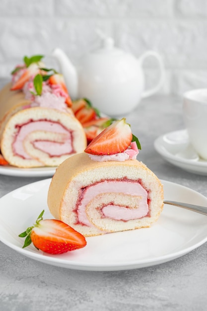 Rolo de bolo com geléia de morangos frescos e queijo creme em um prato branco sobre fundo cinza