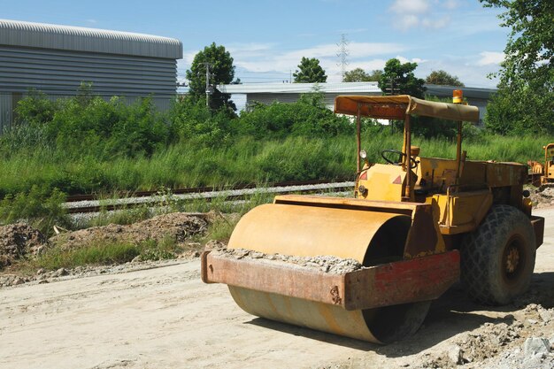 Rolo de estrada Obras de construção na nova estrada preparando-se antes do trabalho de compactação do asfalto Grande caminhão de rolo Bulldozer amarelo em estradas vazias sem ninguém como meio-dia céu azul claro ao longo da ferrovia de trem