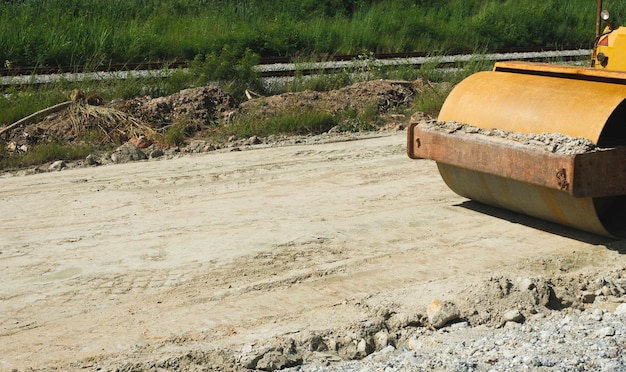 Rolo de estrada Obras de construção na nova estrada preparando-se antes do trabalho de compactação do asfalto Grande caminhão de rolo Bulldozer amarelo em estradas vazias sem ninguém como meio-dia céu azul claro ao longo da ferrovia de trem