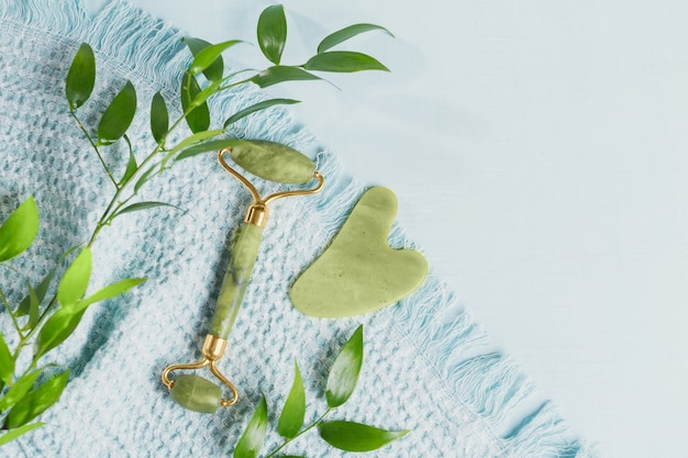 Rolo de face de jade verde e raspador de gua sha com folhas em fundo azul claro