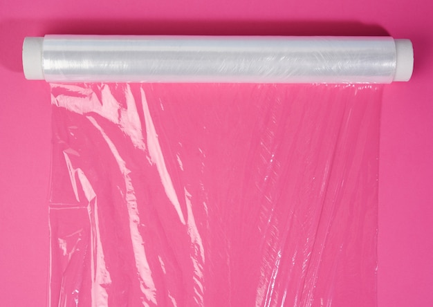 Foto rolo de filme plástico transparente em fundo rosa para embalagem de produtos, vista superior