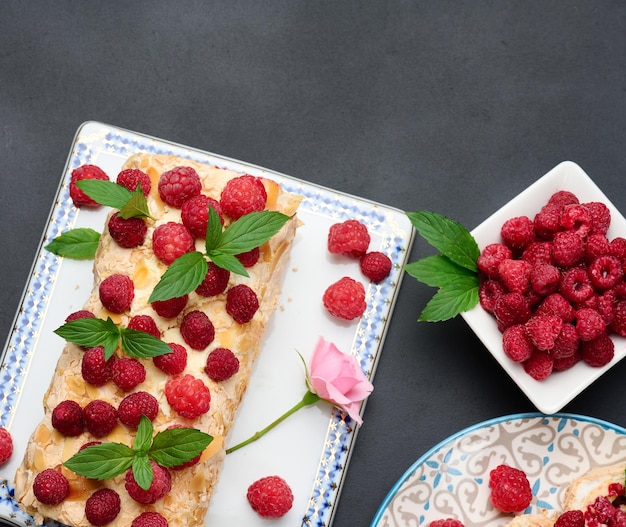 Rolo de merengue assado com creme e framboesa vermelha fresca em uma placa de madeira preta