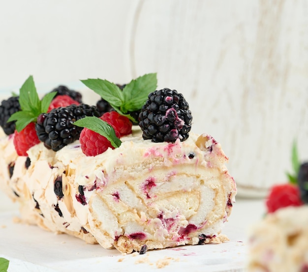 Rolo de merengue assado com creme e frutas frescas em uma deliciosa sobremesa de tábua de madeira branca