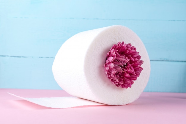 Rolo de papel higiênico com sabor e uma flor rosa em uma mesa rosa. Papel higiênico com um cheiro. Conceito de higiene