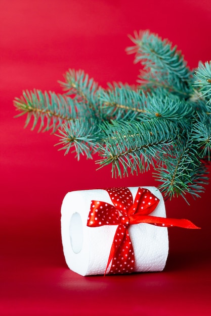 Rolo de papel higiênico como presente de natal sob um galho de uma árvore de natal em um fundo vermelho