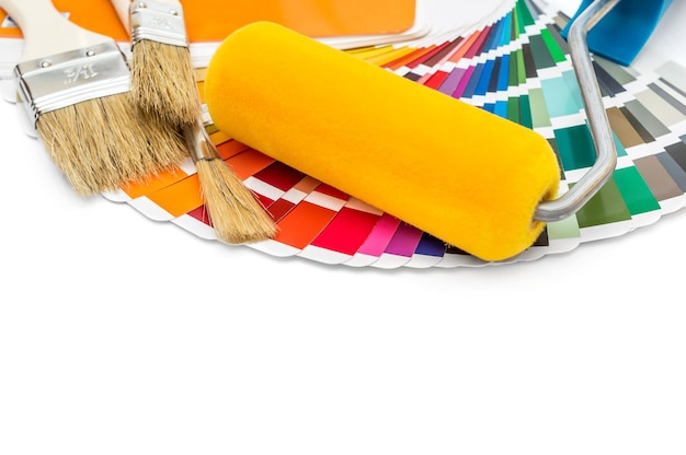Rolo de pintura com pincéis e livro de amostras de cores sobre fundo branco