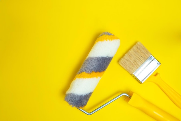 Rolo de pintura e pincel para pintar e reparar paredes em fundo amarelo