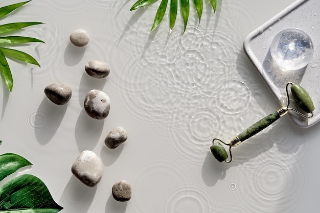 Rolo de rosto de jade para terapia de massagem facial de beleza Folhas exóticas palmeira e monstera Produtos naturais de cuidados com a pele feitos por si mesmo Plano em fundo branco Anéis de água sombras de círculos salpicos