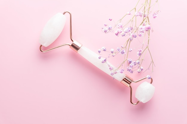 Foto rolo de rosto e flor de gipsófila em fundo rosa. ferramenta de massagem para o cuidado da pele facial, tratamento de beleza spa em casa.