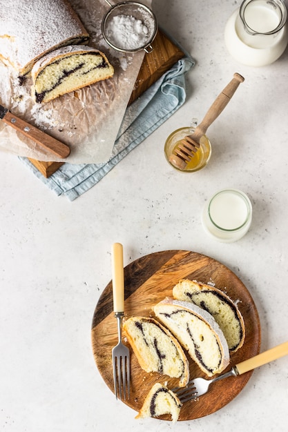 Rolo de semente de papoula ou strudel na placa de madeira polvilhada com açúcar de confeiteiro.