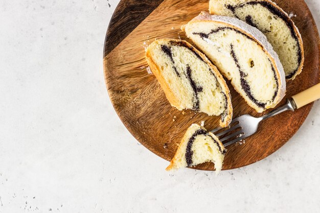 Rolo de semente de papoula ou strudel na placa de madeira polvilhada com açúcar de confeiteiro.