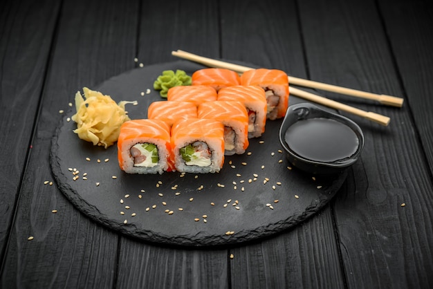 Rolo de sushi com salmão, queijo creme no preto.