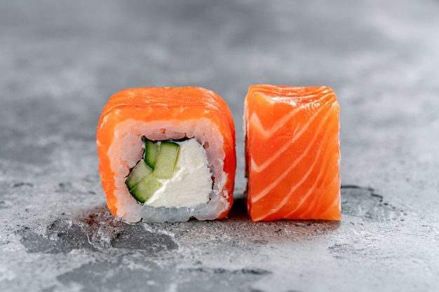 Foto rolo de sushi da filadélfia com salmão, queijo e pepino em um fundo de pedra cinza. o conceito do menu japonês.