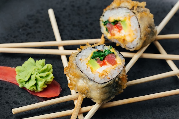 Rolo de sushi de atum caseiro com abacate e queijo em um empanado crocante em um prato de pedra escura.