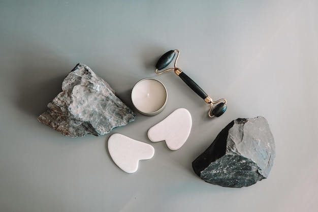 Rolo facial de jade e raspador de gua sha e pedra natural em um fundo cinza Conjunto de massagem facial para terapia de levantamento feito de pedras naturais Vista superior plana