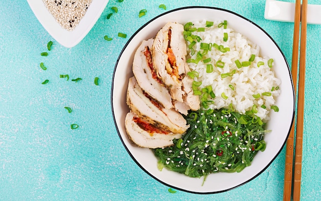 Rolos de frango, arroz, chuka e cebola verde em uma tigela branca com pauzinhos