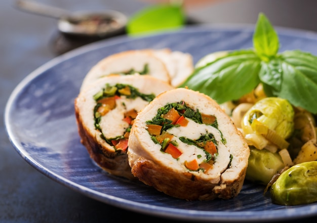 Rolos de frango com verduras, guarnecidos com couve de bruxelas estufada, maçãs e alho-poró em um prato azul.