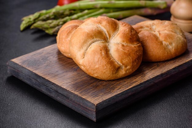 Rolos de pão redondos crocantes conhecidos como Kaiser ou Viena rola em uma tábua de corte