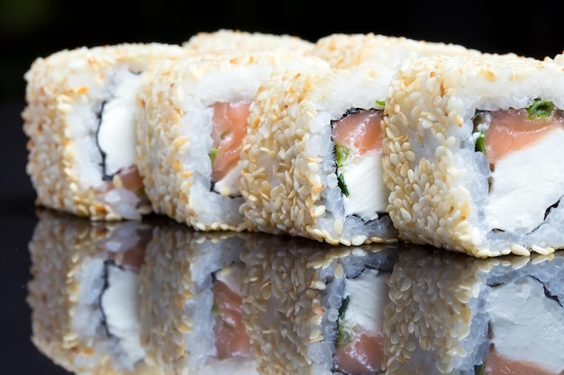 Foto rolos de sushi agitar chizu com gergelim em um fundo preto.