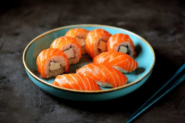 Rolos de sushi caseiro filadélfia e nigiri em uma placa azul sobre uma superfície preta.